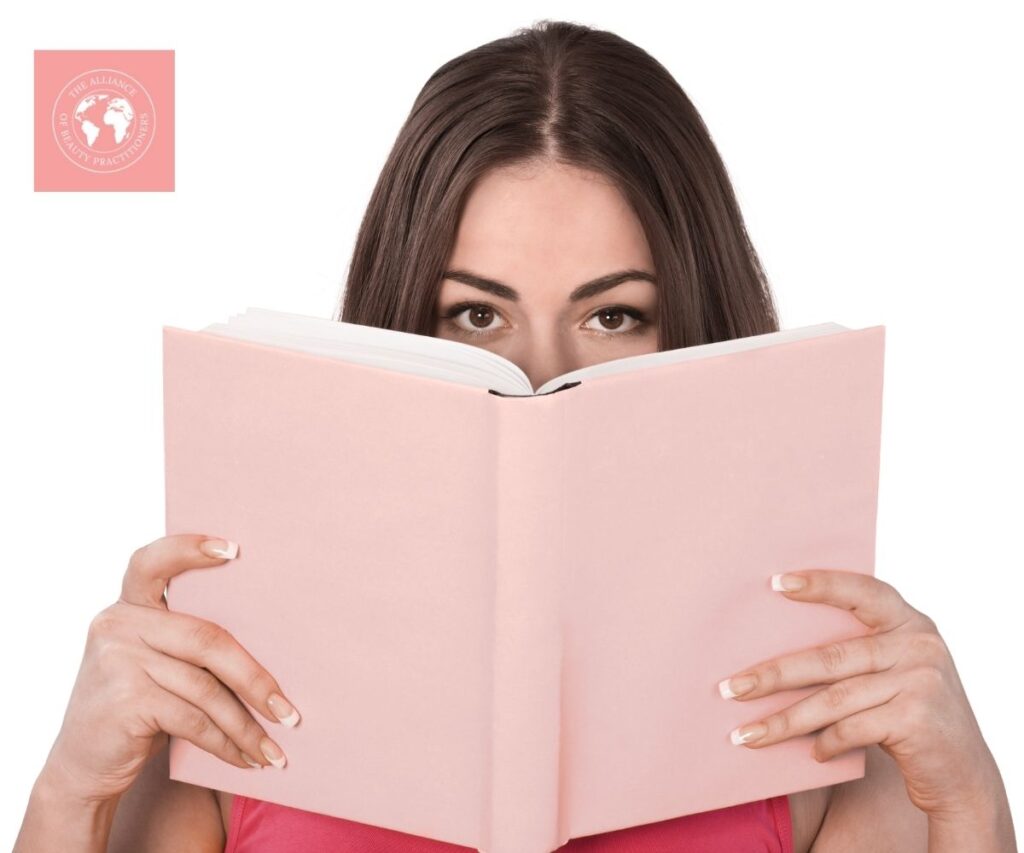 A lady peeping over the top of one of our pink beauty training manuals