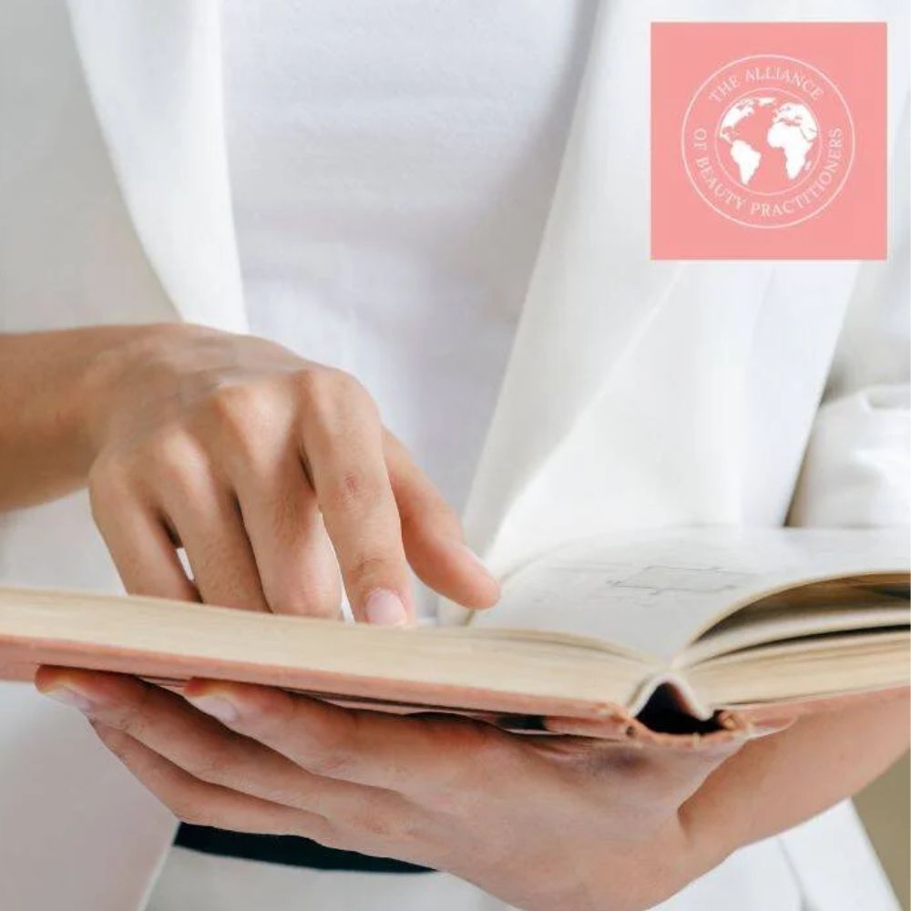 A lady in white jacket and top reading one of our beauty training manuals