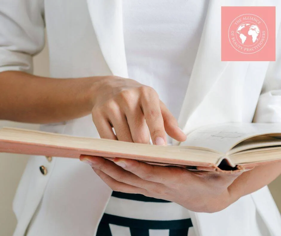 A lady in white jacket and top reading one of our beauty training manuals